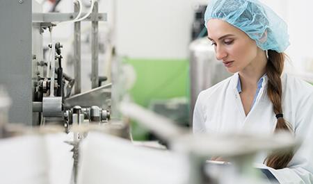 机械工业——快乐的女员工戴着防护帽和白色的实验室大褂，在一个现代工厂作为制造工程师工作